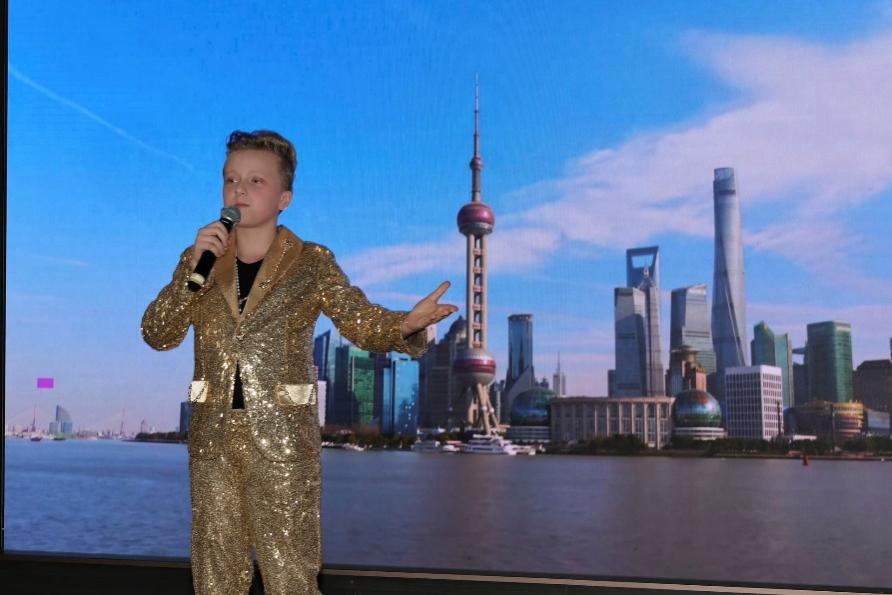 A child in a suit with a microphone in front of a city

Description automatically generated